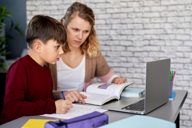 Le garçon fait ses devoirs pendant que la mère enseigne à la maison.