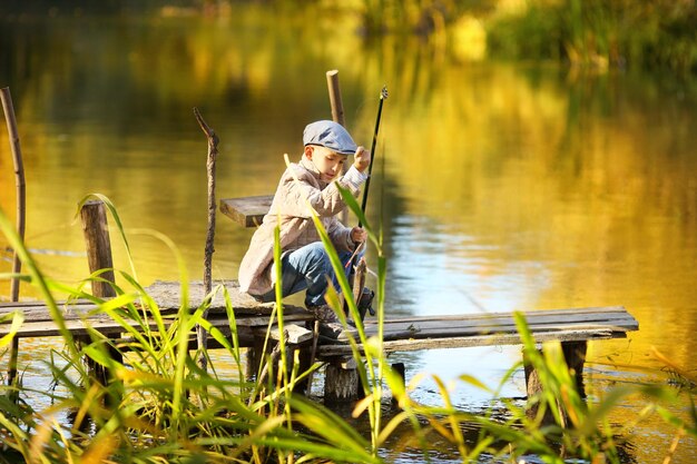 Le garçon avec un filet de pêche se penche sur une balustrade en bois de dock