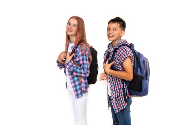 Garçon et fille adolescent 11 ans écolier et écolière regardant la caméra sur fond blanc avec des sacs à dos et souriant. Habillé en chemise à carreaux, chemise blanche