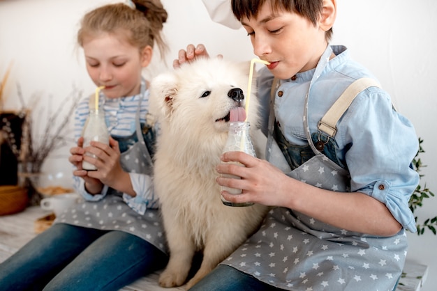 Un garçon et une fille boivent du lait avec une paille et un chiot lèche les gouttes d'une bouteille