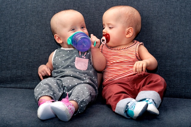 Photo garçon et fille jusqu’à l’année boivent de l’eau d’une bouteille posée sur le canapé. le concept de jumeaux dans la famille.