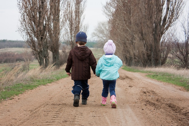 Garçon et fille marchent le long de la route en se tenant la main.