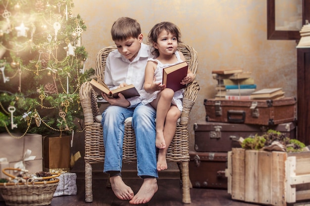 Garçon et fille mignons de bébés dans une chaise lisant un livre dans un intérieur rétro de Noël