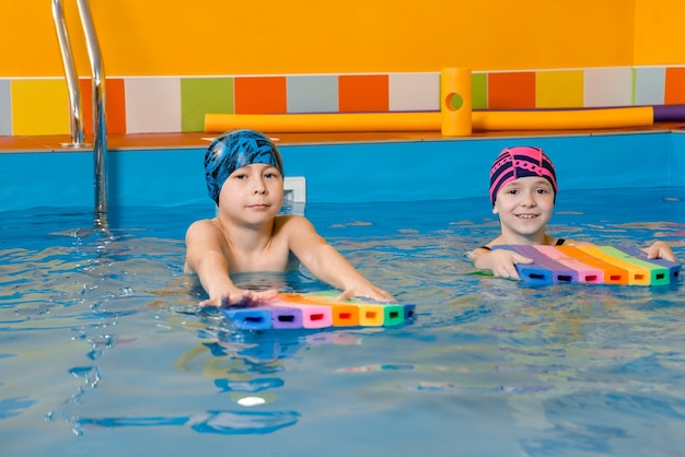 Garçon et fille portant un maillot de bain utilise un coussin en mousse pour pratiquer la natation dans la piscine