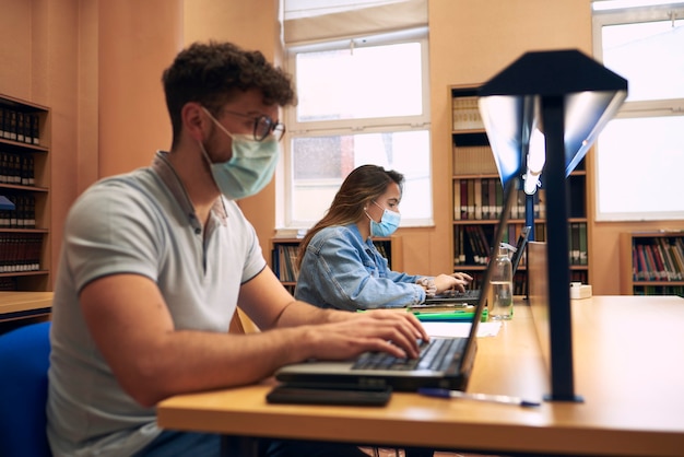 Un garçon et une fille portant des masques utilisent des ordinateurs portables dans la bibliothèque