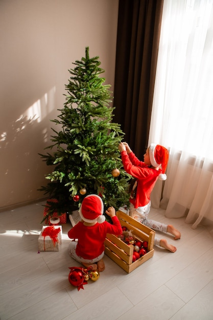 garçon et fille en pyjama rouge décorent l'arbre de Noël dans le concept d'hiver du salon