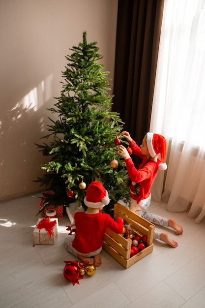 garçon et fille en pyjama rouge décorent l'arbre de Noël dans le concept d'hiver du salon