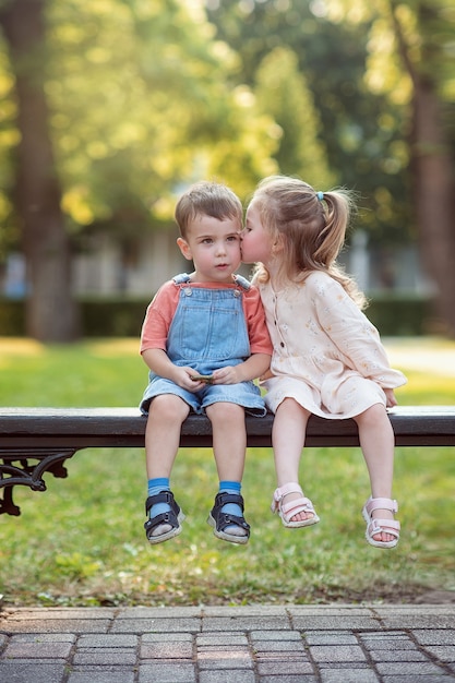 Un garçon et une fille sont assis sur un banc dans le parc une fille embrasse un garçon sur la joue