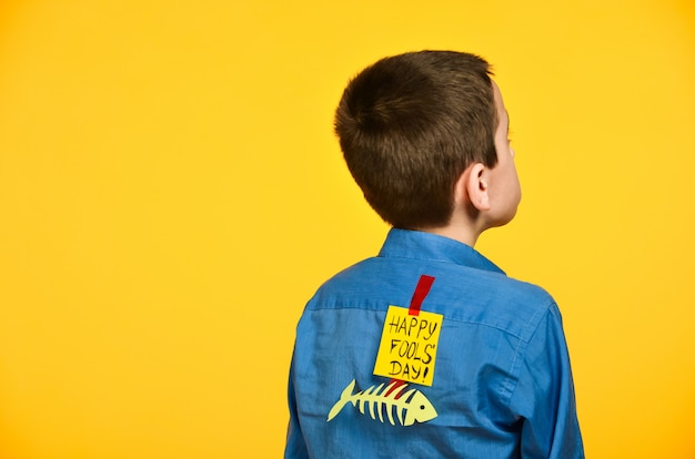 Photo le garçon sur fond jaune dans une chemise bleue avec un ruban adhésif et un morceau de papier sur le dos