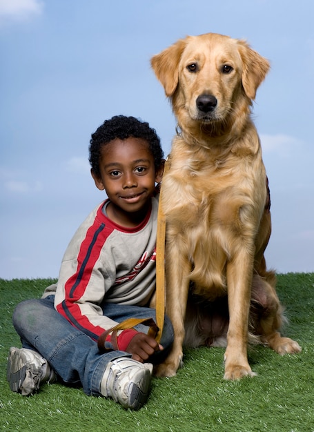 Garçon Et Golden Retriever Assis Sur L'herbe Contre Un Ciel Bleu