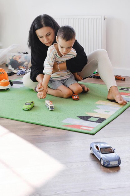 Photo un garçon handicapé jouant à des voitures jouets avec sa mère à la maison, un enfant atteint de paralysie cérébrale s'amusant sur le tapis.