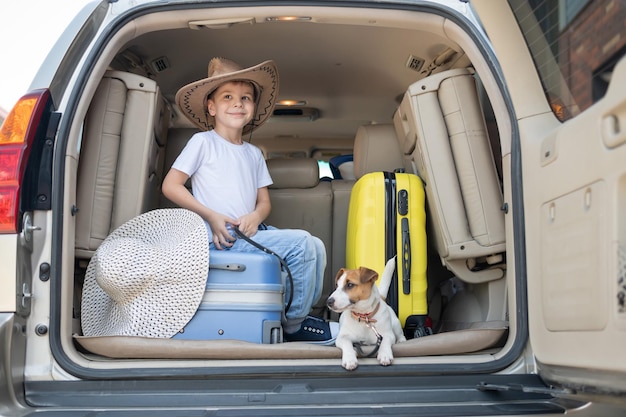 Un garçon heureux dans un chapeau de cow-boy et un chiot jack russell terrier voyagent en voiture Un enfant et un petit chien drôle sont assis dans le coffre et sont prêts pour les vacances d'été Voyage indépendant Meilleurs amis