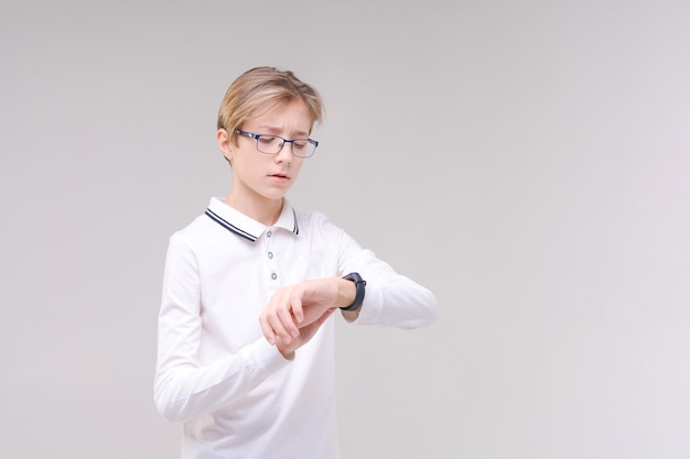 Un garçon heureux dans des verres et une chemise regarde sa montre ou son tracker de fitness