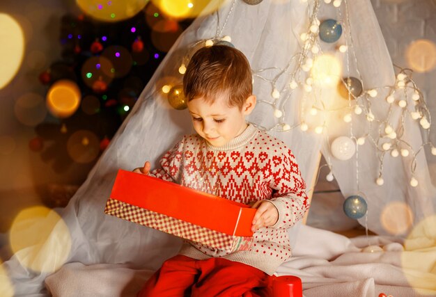 Un garçon heureux déballant ses cadeaux de Noël à la maison a surpris un enfant mignon