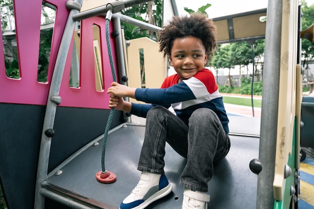 Garçon heureux d'enfant avec des cheveux afro dans l'aire de jeux dans le parc