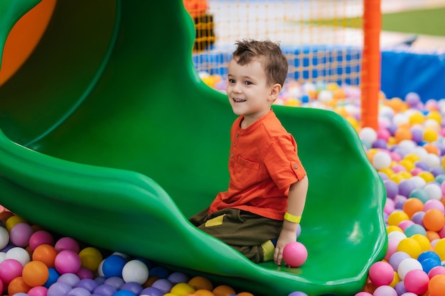 Un garçon heureux joue dans une piscine sèche avec des balles colorées et descend un toboggan Centre de divertissement pour enfants Loisirs actifs