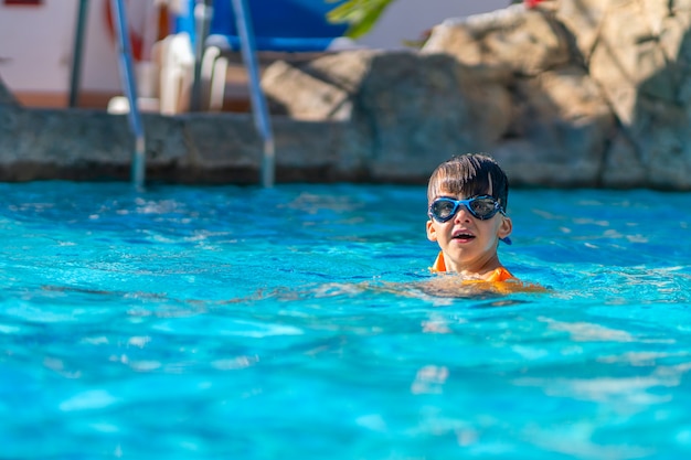 Photo un garçon heureux en lunettes de natation et volants de bras dans une piscine extérieure.