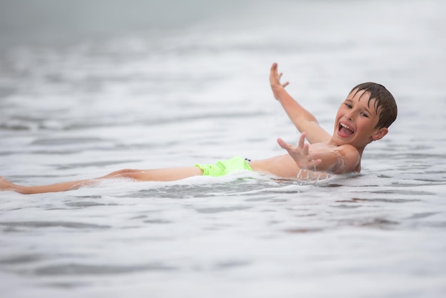 Un garçon heureux nage dans la mer joue avec les vagues et les éclaboussures