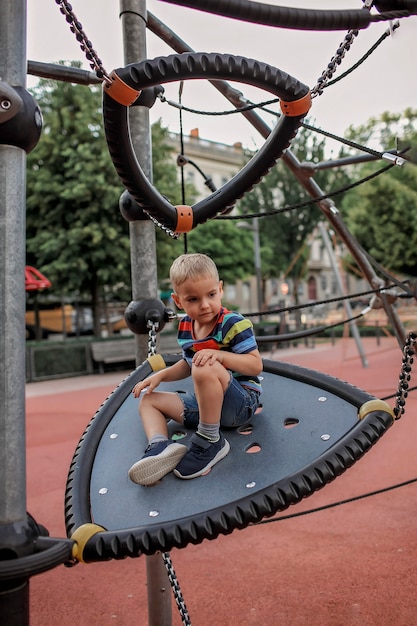 Garçon heureux se reposer sur l'aire de jeux dans le parc local pendant son voyage