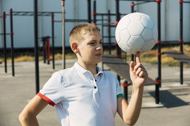 Garçon heureux en t-shirt blanc travaillant sur le terrain de sport et un ballon de sport.