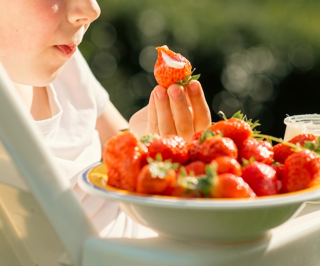 Un garçon de huit ans mange des fraises avec du yaourt en été dans la cour