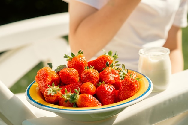 Un garçon de huit ans mange des fraises avec du yaourt en été dans la cour