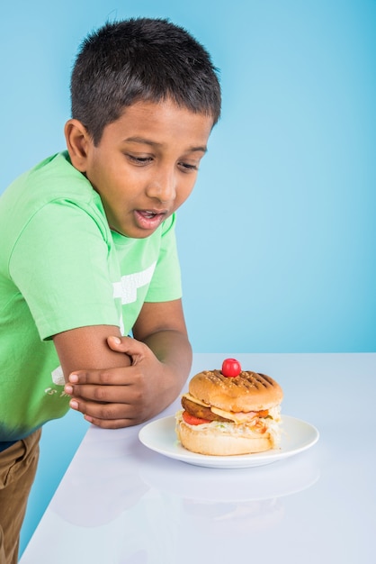 Garçon indien mignon mangeant un hamburger, petit garçon asiatique et hamburger, sur fond bleu