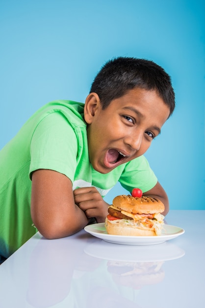 Garçon indien mignon mangeant un hamburger, petit garçon asiatique et hamburger, sur fond bleu