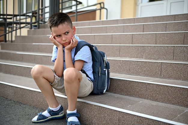 Garçon inquiet bouleversé avec sac à dos assis dans les escaliers près de l'école. L'intimidation, la solitude, les difficultés d'étude. Retour au concept de l'école