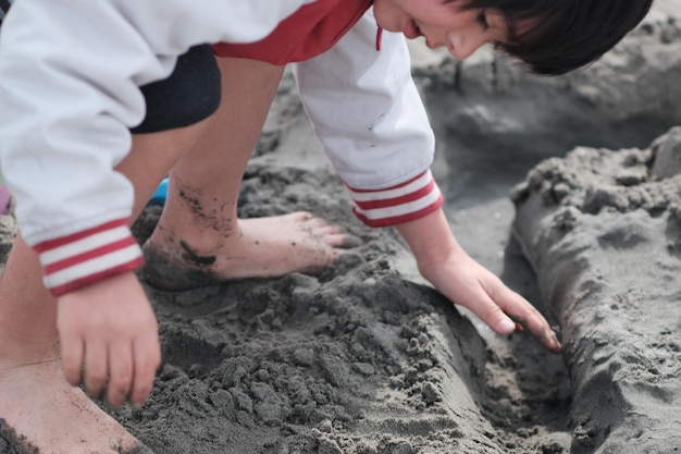 Photo un garçon insouciant jouant avec du sable sur la plage