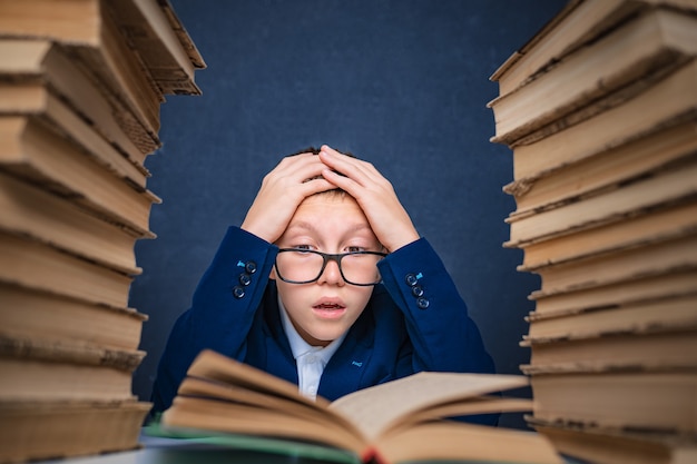 Garçon intelligent dans des verres assis entre deux piles de livres et lire attentivement le livre