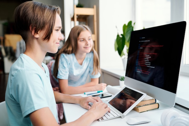 Garçon intelligent et son camarade de classe à la recherche de données sur un écran d'ordinateur alors qu'ils étaient tous deux assis par un bureau en classe