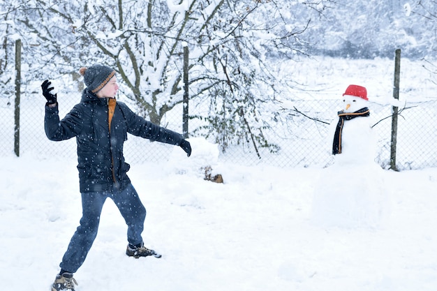 Garçon jouant à la bataille de boules de neige à côté d'un bonhomme de neige, activités d'hiver amusantes