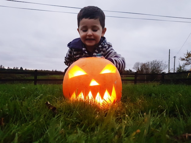 Un garçon jouant avec une citrouille illuminée sur le champ contre le ciel pendant Halloween