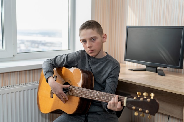 Photo garçon jouant de la guitare assis près de la fenêtre en classe de musique