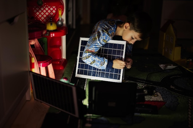 Garçon jouant à la maison pendant une panne d'électricité à l'aide d'un éclairage alternatif avec panneau solaire