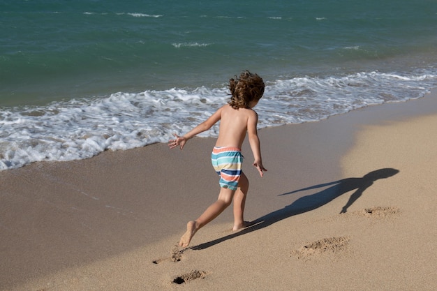 Garçon jouant sur la plage pendant les vacances d'été Enfants dans la nature avec du beau sable de mer et bleu courant dans l'eau de mer