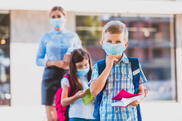 Un garçon joyeux aux yeux souriants ajuste son masque médical en regardant la caméra Portrait d'écolier après la fin des cours