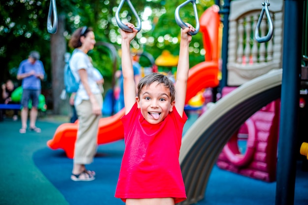 Un garçon joyeux est engagé sur des anneaux de gymnastique dans le parc en vacances L'enfant fait du sport