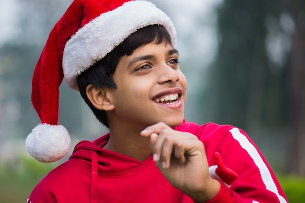 Un garçon joyeux et mignon avec une casquette de père Noël et un t-shirt rouge souriant joyeusement et regardant à distance