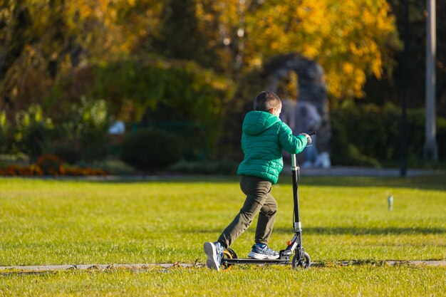 Un garçon joyeux roule rapidement sur un scooter dans un parc de la ville