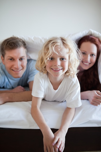 Garçon joyeux sous la couverture de lit avec ses parents