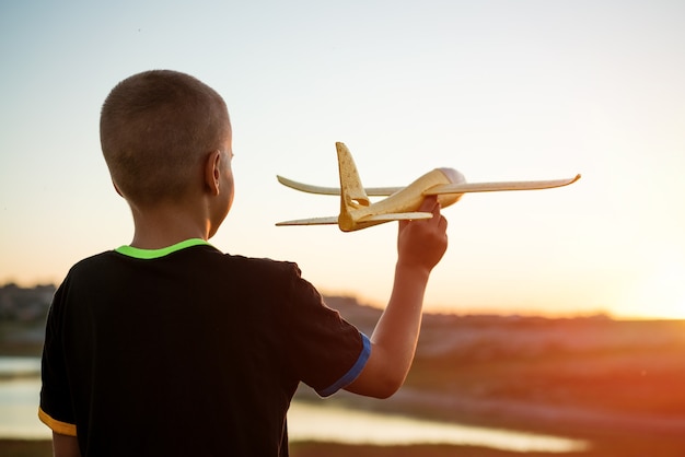 Un garçon lance un avion jouet en été au coucher du soleil un enfant joue avec un avion jouet rêve d'un voyage...