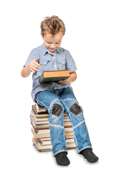 Un garçon avec un livre assis sur une pile de livres sur un fond blanc isolé