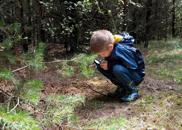 Un garçon avec une loupe à la main est un étudiant en nature dans la forêt