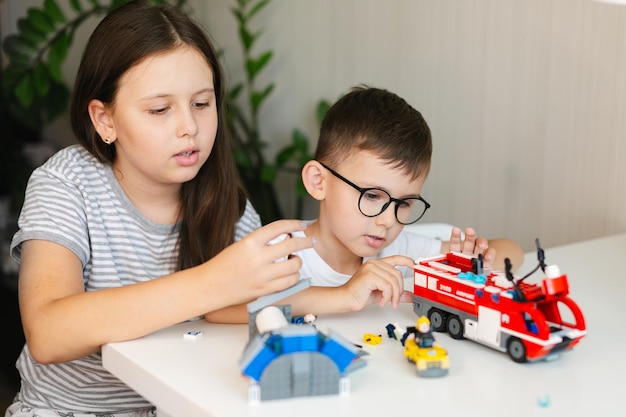 Photo un garçon en lunettes et une fille jouent avec des briques de construction de jouets colorés