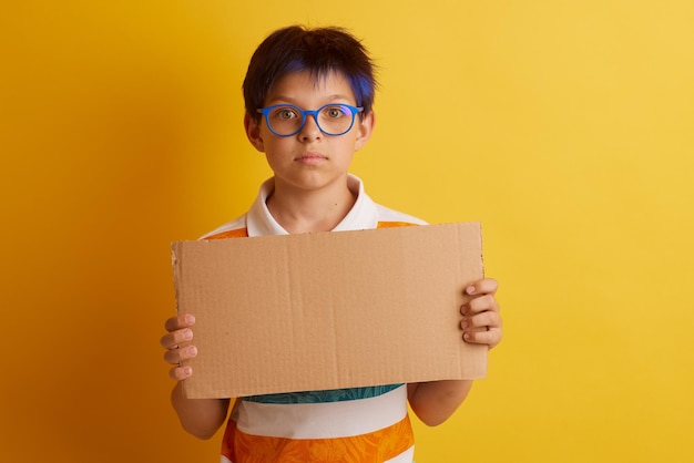 Un garçon avec des lunettes sur fond jaune avec différentes émotions tient une bannière en carton