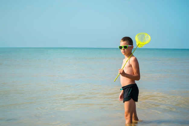 Garçon à lunettes de soleil se tient dans la mer avec un filet à papillons.