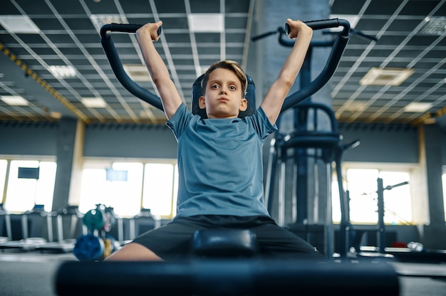 Garçon sur machine d'exercice, vue de face, formation en salle de gym. Jeune en club de sport, soins de santé et mode de vie sain, écolier en entraînement, jeunesse sportive