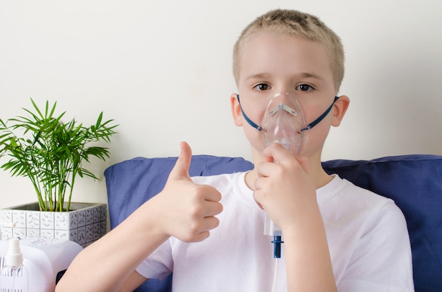 Garçon malade respirant à travers le masque de l'inhalateur et gesticulant les pouces vers le haut